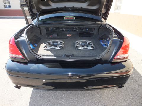 2003 Ford Crown Victoria - Rear view of a black sedan trunk holding two angled subwoofers and amps on a custom carpeted panel