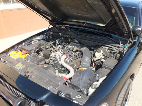 2003 Ford Crown Victoria - Hood-up view of a dark sedan engine bay with the air filter housing and accessory belts visible
