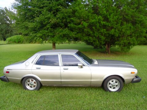 1978 Nissan Maxima - A 1978 Nissan Maxima sedan is shown parked on a grassy lawn with trees in the background.
