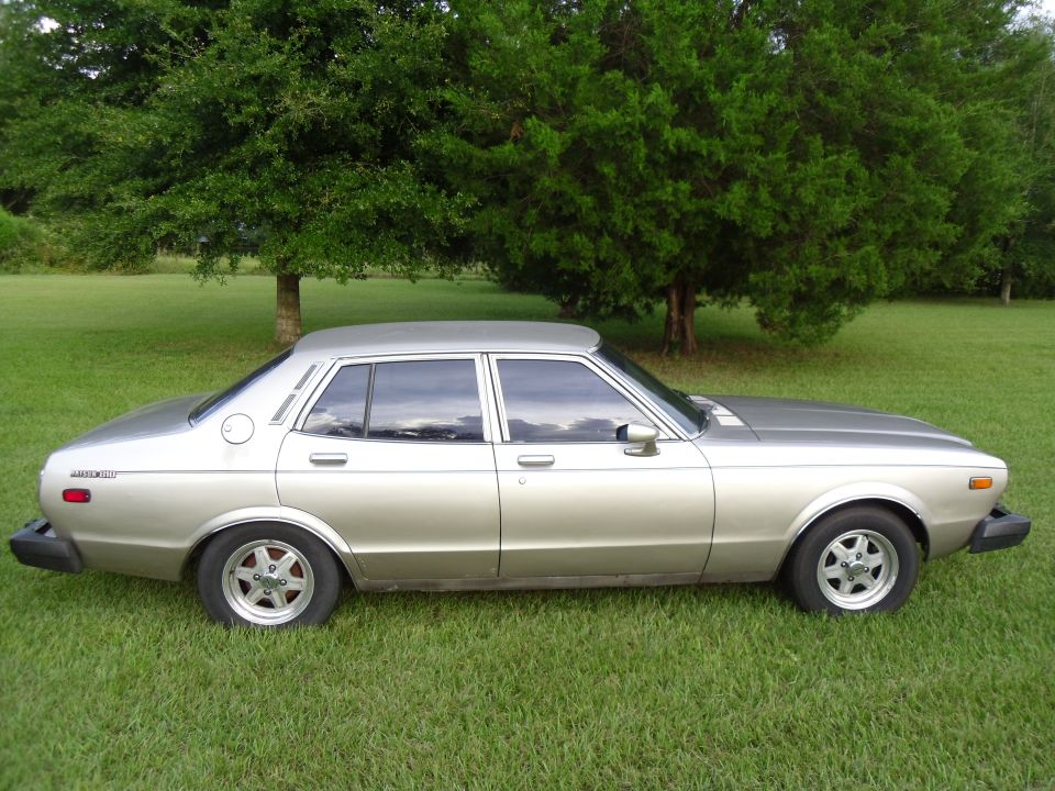 Silver and gold four-door sedan parked on grass under trees, side profile