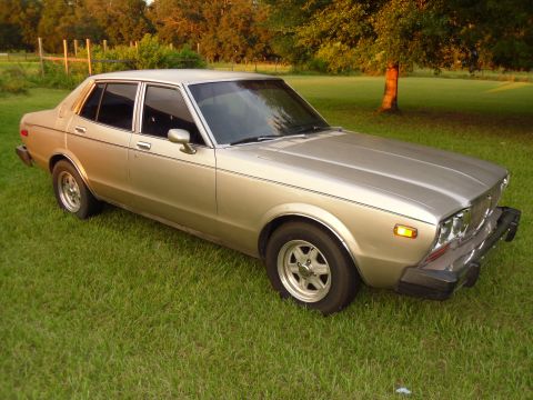 1978 Nissan Maxima - A vintage sedan sits on a grassy lawn during the golden hour, with trees and a fence visible in the background.