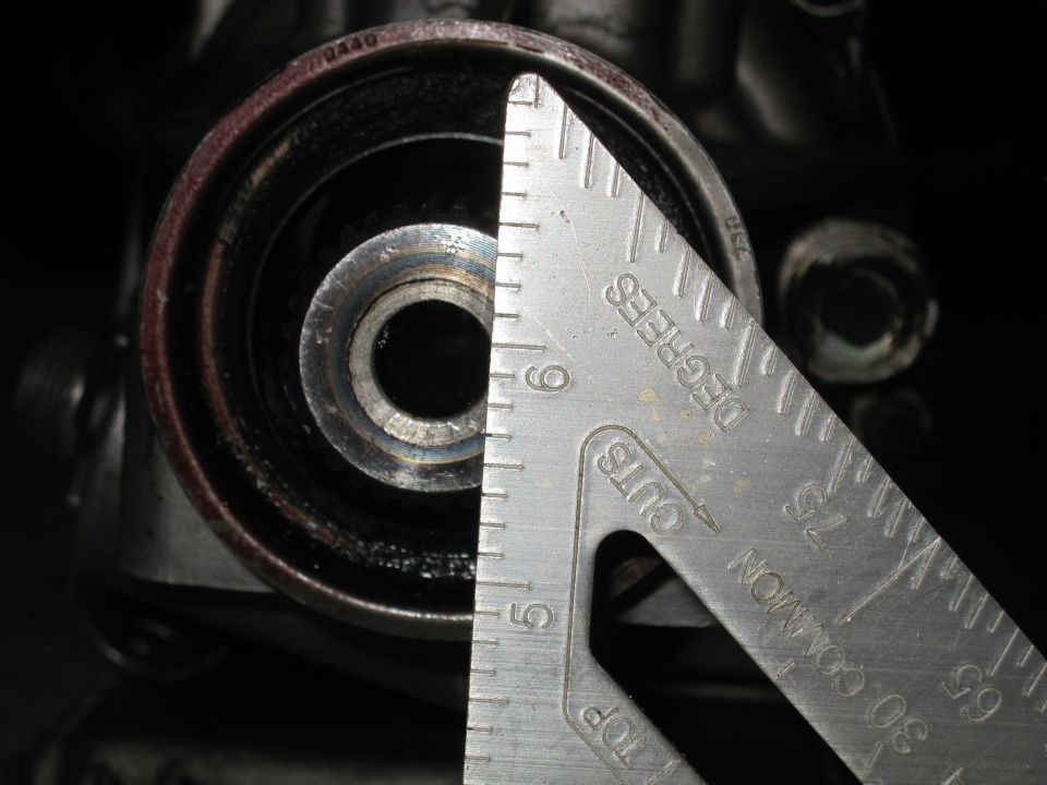 Close-up of a metal part, possibly a pulley or bearing, being measured with a metal ruler. Ruler markings are visible