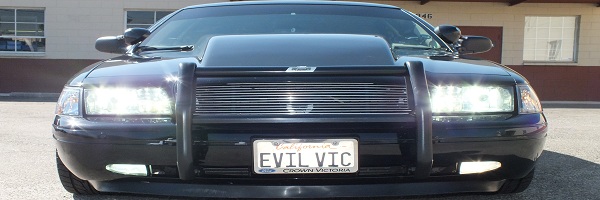 Front grille of black Ford Crown Victoria with push bar and EVIL VIC license plate, headlights on