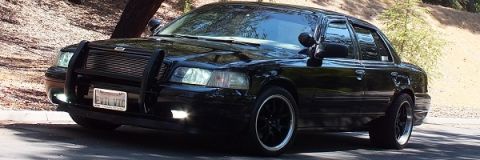 2003 Ford Crown Victoria - Black Crown Victoria with brush guard and lit headlights staged in dappled shade under a tree