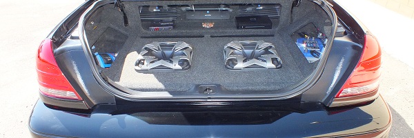 Open trunk of black sedan with two angled subwoofers, amplifiers and Soundstream Epicenter