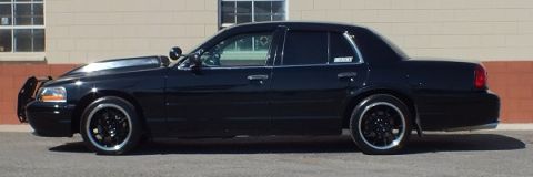 2003 Ford Crown Victoria - Full side view of a lowered black Crown Victoria with brush guard against a beige wall
