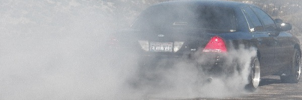 Black Ford sedan doing a burnout in heavy tire smoke with EVIL VIC license plate visible