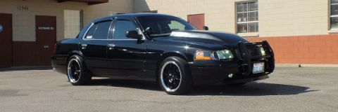 2003 Ford Crown Victoria - Front three-quarter of a lowered black Crown Victoria with brush guard near a warehouse