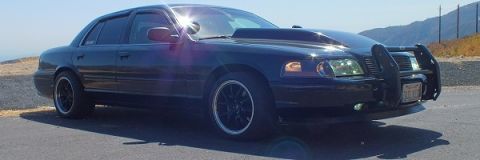2003 Ford Crown Victoria - Front three-quarter of a black Crown Victoria with brush guard, sunlight flaring off the hood