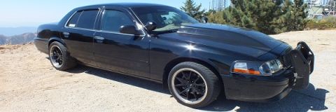 2003 Ford Crown Victoria - Side view of a black Mercury sedan parked on a mountain overlook, black alloy wheels and front push bar