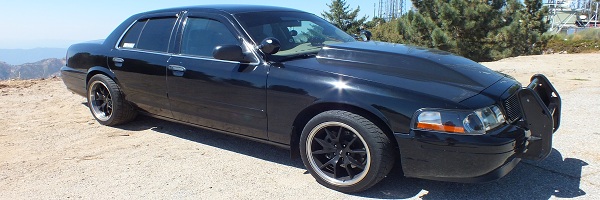 Black Mercury full-size sedan profile on a hilltop, black wheels, push bar on front bumper