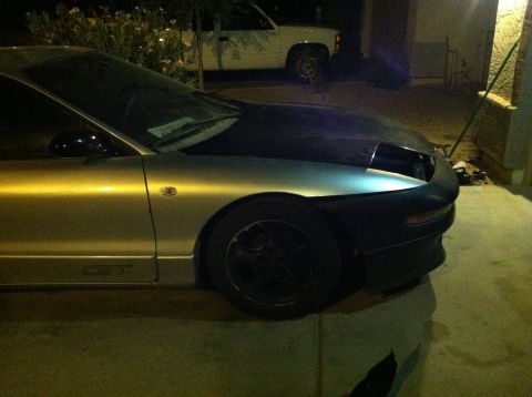 1993 Ford Probe - A silver car with a black hood and missing headlight is parked next to a white pickup truck.