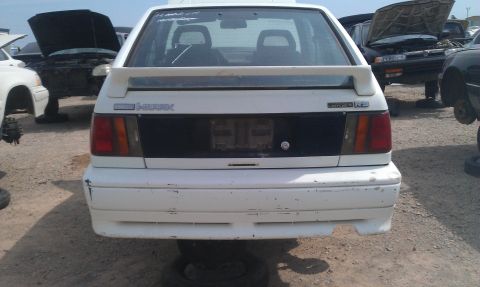 1991 Ford Festiva - A white hatchback sits in a junkyard with other vehicles.