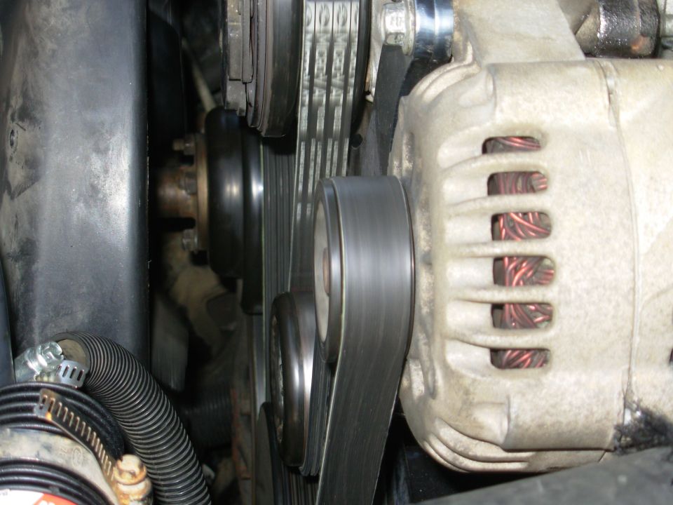 Engine bay close-up: alternator, serpentine belt and pulleys with hose clamps