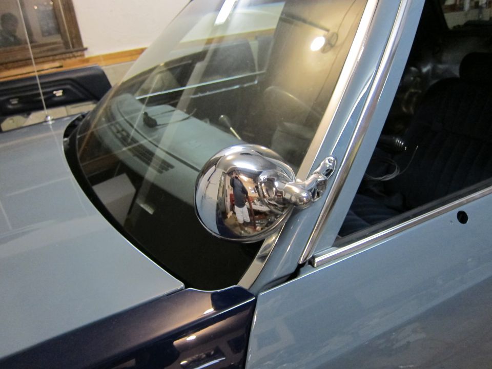 Close-up of a chrome side mirror on a light blue car. Interior and dashboard visible through the windshield