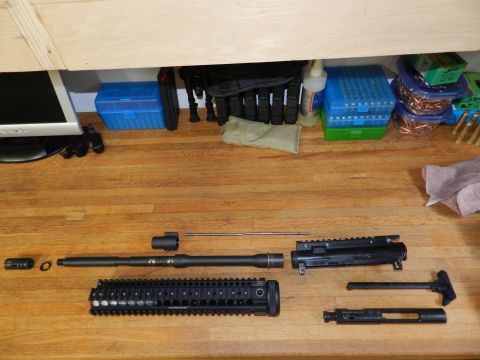 1996 Ford Bronco - Disassembled AR-15 upper receiver parts laid out on a wooden table. Includes barrel, handguard, and bolt carrier group.
