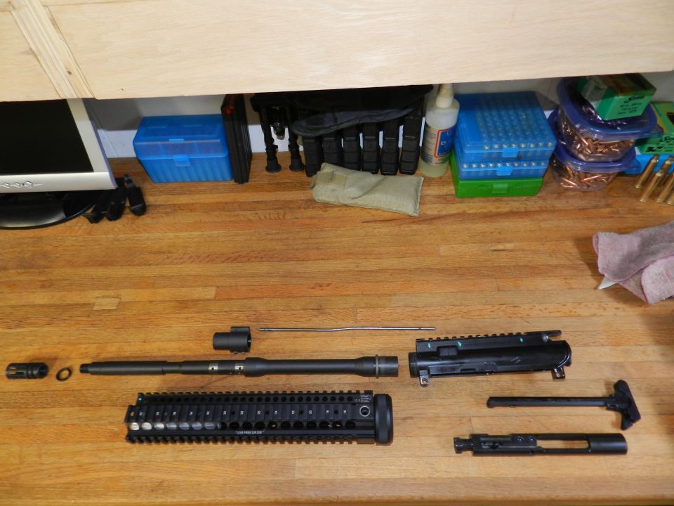 Disassembled AR-15 upper receiver parts on a wooden surface. Includes barrel, handguard, bolt carrier group, and charging handle