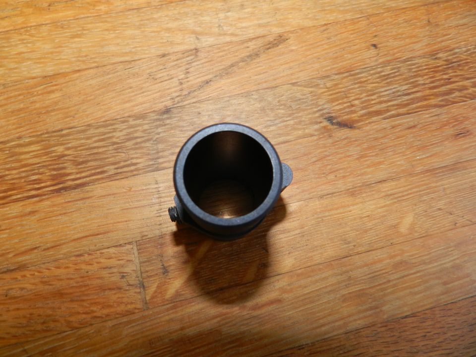 Close-up of a black metal pipe fitting with a clamp screw, resting on a wooden surface