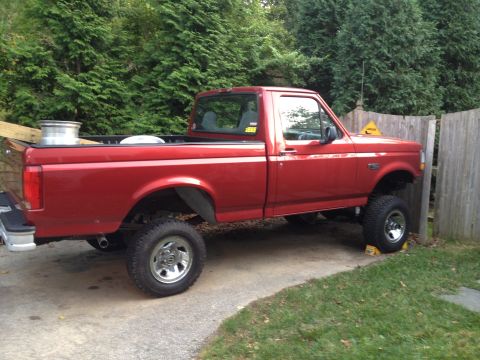 1996 Ford F-150 - This red 1996 Ford F-150 pickup truck is shown from the side, a lifted suspension and aftermarket wheels.