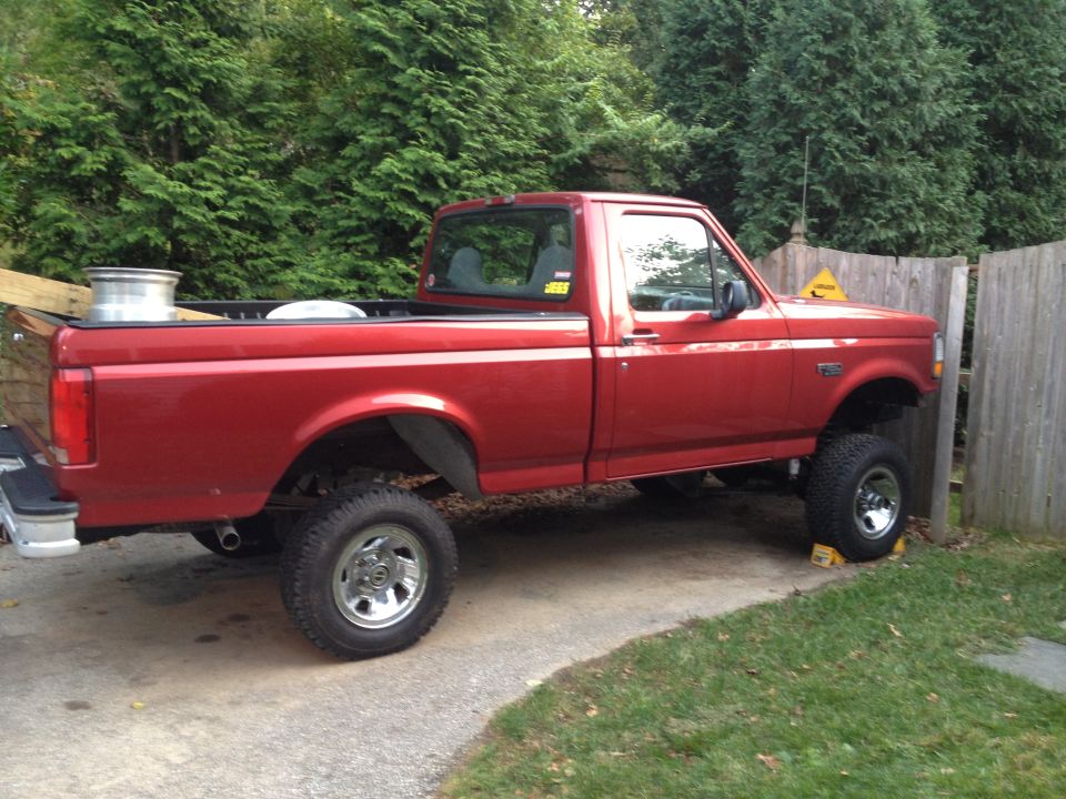 Red 1996 Ford F-150 pickup truck, side view, lifted with aftermarket wheels