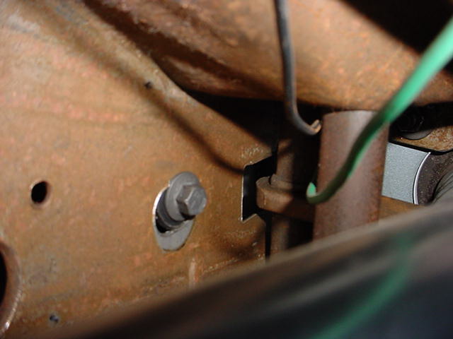 Close-up of rusty vehicle frame with a bolt and green wire