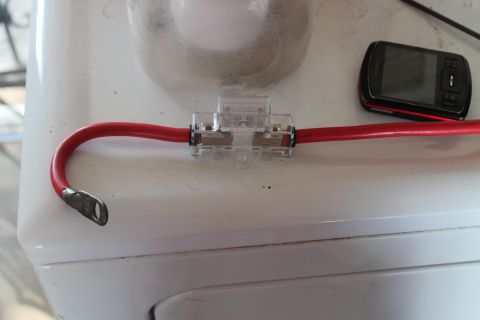 1990 Ford Bronco - A close-up of an in-line fuse holder connected to a red wire, with a cell phone nearby.