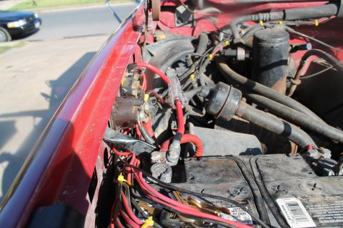 1990 Ford Bronco - The engine bay of a red vehicle shows the battery and complex wiring system, with another car in the background.