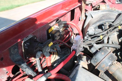 1990 Ford Bronco - Close-up view of the engine bay wiring and battery terminals, red cables and a clear fuse holder.