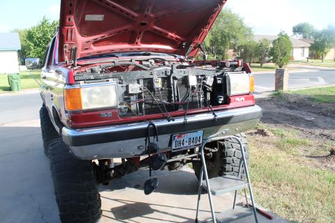 1990 Ford Bronco - Front view of a red lifted pickup truck with its hood open, revealing the engine compartment and grille.