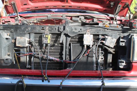 1990 Ford Bronco - Close-up view of the engine bay of a red vehicle, showing the radiator and various electrical components and wiring.