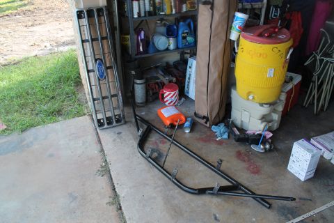1990 Ford Bronco - A Ford grille and brush guard are stored in a garage with various other items.