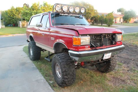 1990 Ford Bronco - This modified Ford Bronco sits high on off-road tires, missing its front grille and sporting a roof-mounted light bar.
