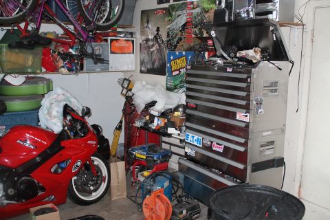 1990 Ford Bronco - A red sport motorcycle is parked in a garage filled with tools, posters, and other items.