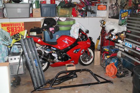1990 Ford Bronco - A red sport motorcycle and a Ford Bronco grille are stored in a cluttered garage with various tools and storage bins.