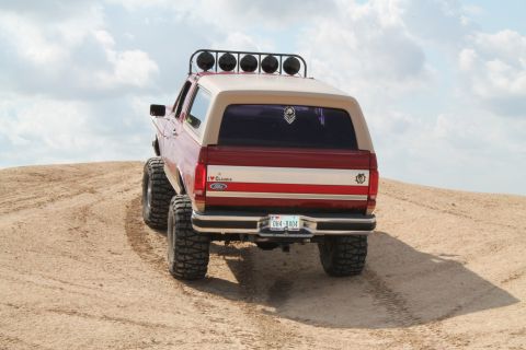 1990 Ford Bronco - This lifted Ford Bronco is shown from the rear, climbing a sandy incline under a cloudy sky.