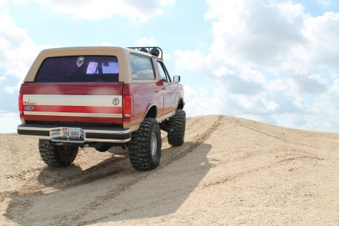 1990 Ford Bronco - This modified Ford Bronco is shown from the rear, ascending a sandy incline under a cloudy sky.
