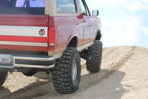 1990 Ford Bronco - Rear view of a lifted 1990 Ford Bronco with large tires, climbing a dirt hill.