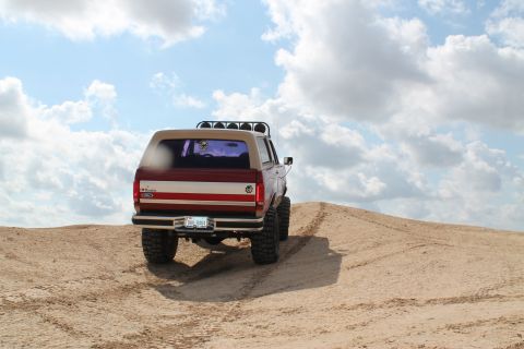 1990 Ford Bronco - This Ford Bronco is climbing a sandy hill with a two-tone paint job and a light bar on the roof.