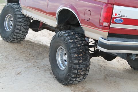 1990 Ford Bronco - Rear view of a lifted red 1990 Ford Bronco, large off-road tires and a personalized decal.