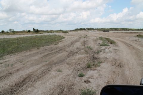 1990 Ford Bronco - A view from a vehicle driving on a dirt road through a dry, open area with sparse vegetation.