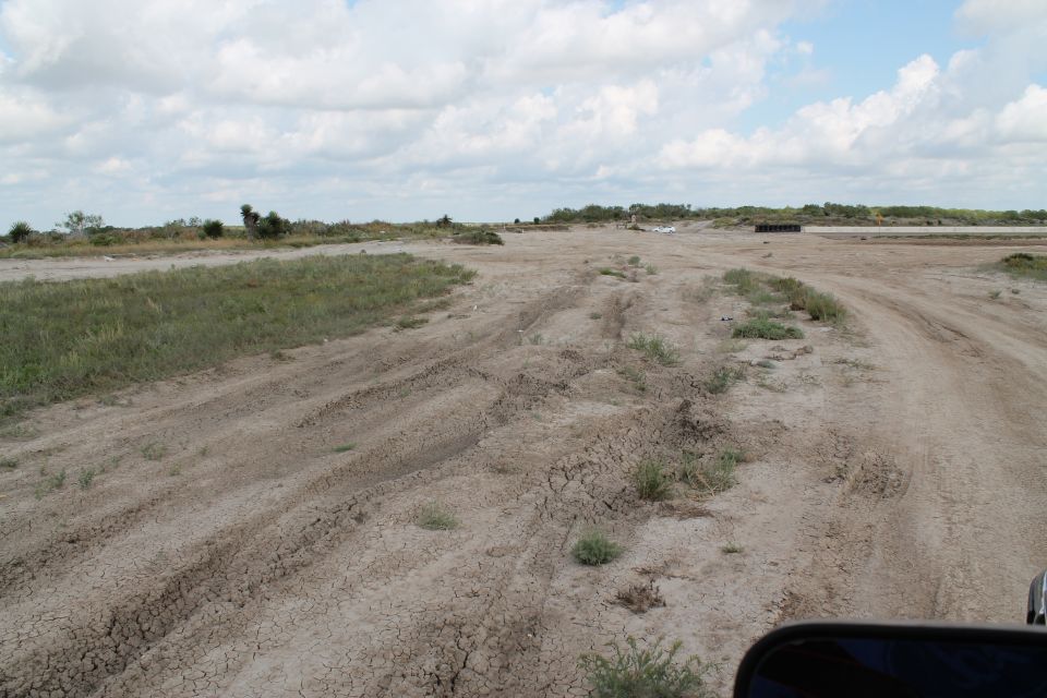Dirt road with tire tracks in a dry, grassy landscape under a cloudy sky