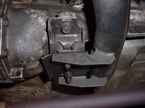 1991 Ford LTD Crown Victoria - Close-up view of an engine mount and exhaust pipe, showing mechanical components and some grease.