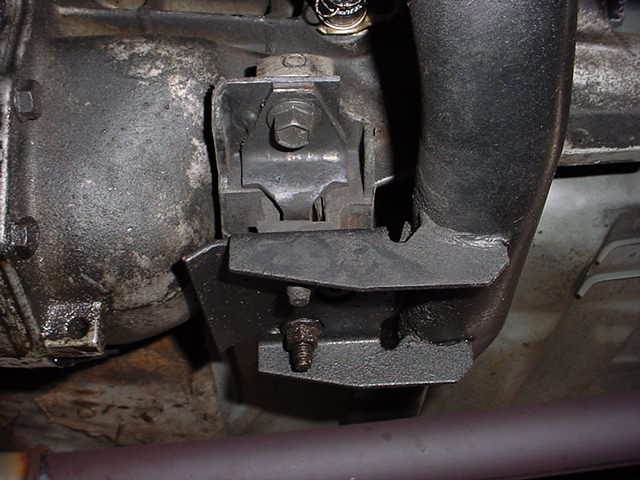 Engine mount bracket attached to a greasy transmission housing with a black exhaust pipe nearby