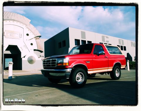 1994 Ford Bronco - A red Ford Bronco from the early 1990s is parked outside a building with a distinctive architectural style.