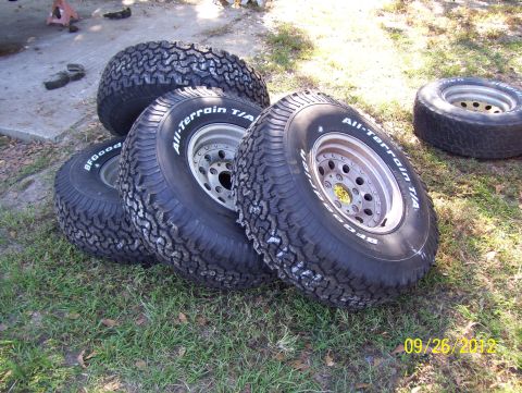 1990 Ford Bronco - Four BFGoodrich All-Terrain T/A tires are piled on the grass next to a concrete surface.