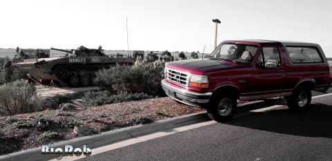1994 Ford Bronco - A Ford Bronco is parked on the side of the road with a military tank in the background.