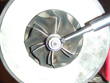 1996 Ford Bronco - Close-up of a turbocharger compressor wheel, with a socket wrench engaged on the central nut.