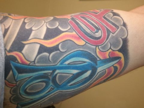 1967 Ford Mustang - A colorful tattoo is inked on an arm, stylized lettering and swirling cloud-like designs.