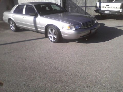 2003 Ford Crown Victoria - A silver 2003 Ford Crown Victoria sedan is parked outside, with a Chevrolet truck visible in the background.