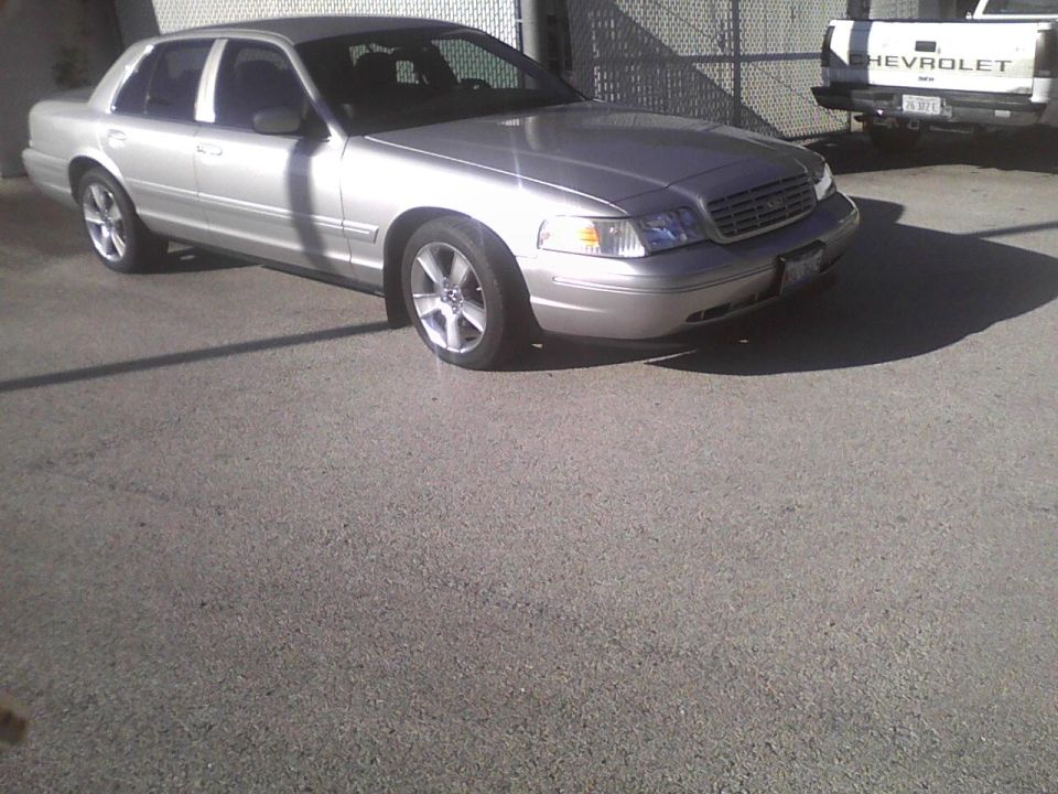 Silver 2003 Ford Crown Victoria sedan parked on asphalt, front quarter view. Some damage visible on the front bumper